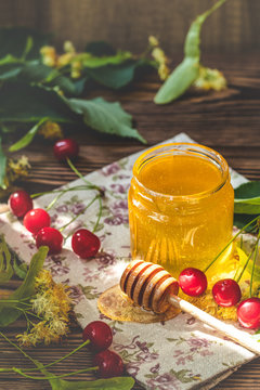 Open glass jar of liquid honey and honey dipper on wooden surface