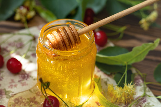 Open glass jar of liquid honey and honey dipper on wooden surface