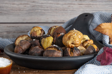 Roasted chestnuts in cast iron grilling pan over rustic wooden board.