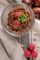 Glass cups of chocolate and chestnuts mousse with roasted almonds and oats decorated with raspberry and mint leaves