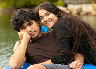 Biracial siblings outdoors relaxing by lake on wooden pier
