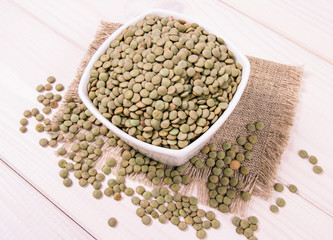 Green lentils in a bowl on a wooden background.