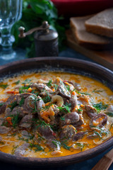 Chicken hearts stewed in sour cream in a clay bowl, selective focus