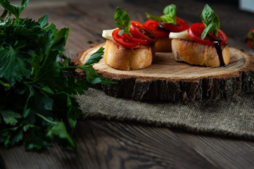 Cheese and tomatoes with basil, bruschettas on a wooden plate, closeup