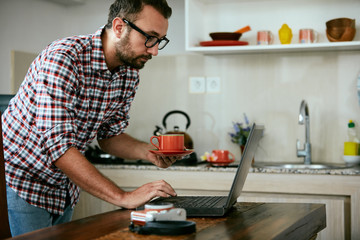Modern bearded man using cellphone and drinking coffee with laptop.