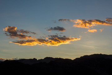 bright white yellow orange clouds in a sunset dark blue sky over the black silhouettes of the mountains