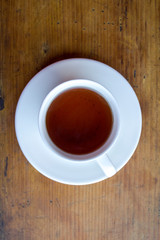 black tea in a white mug on a saucer on the wooden surface of the table top view