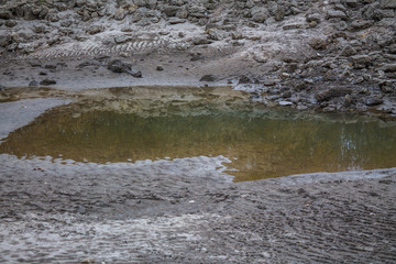 Dirty orange water in the river. The coast with stones is reflected in dirty water. Overcast weather