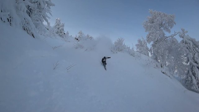 Freerider jumping off a cliff and landing drowning in the snow. super slow motion video on the background of beautiful forest