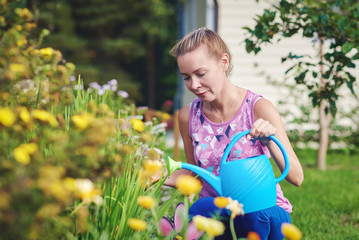 Young Caucasian woman watering flowers at a household plot. © Artem