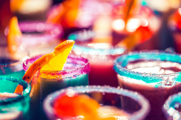 Fototapeta na wymiar Blurred glasses of colorful neon cocktails with sugar rims background, party concept with copy space