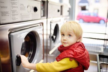 A little boy loads clothes into the washing machine in public laundrette