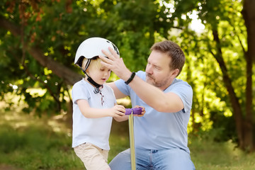 Middle age father helping his little son to put his helmet