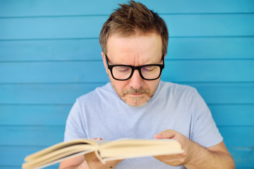 Portrait of mature man with big black eye glasses trying to read book but having difficulties...