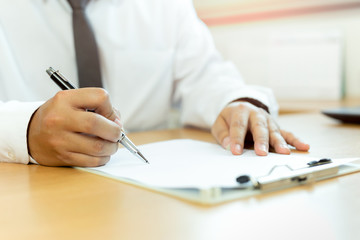 Businessman signing contract paper with pen in office desk.