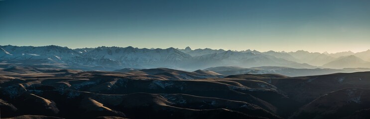 Panoramic landscape on Caucasus mountain range covered with snow and valley with yellow grass during autumn sunset
