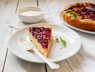 Homemade cherry pie served with cream on a light background with cherry leaves and flowers.