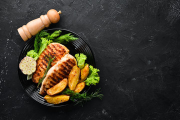 Baked chicken fillet with carrot and vegetables on a black stone background. Top view. Free copy...