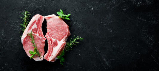 Raw steak on the bone. Meat with spices and herbs. On a black stone background. Top view. Free copy...