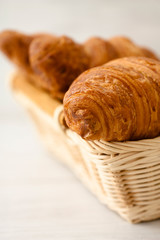 Freshly baked croissants in a wicker basket on a light background.