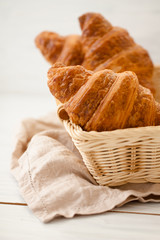 Freshly baked croissants in a wicker basket on a light background.