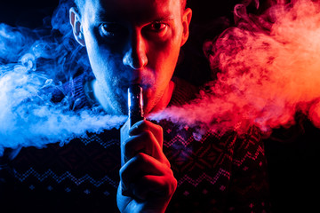 Portrait of a man with a shadow on a serious face  with a colored backlight of blue and red smoking...