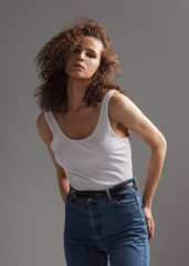 young curly woman in jeans and white t-shirt on studio gray background