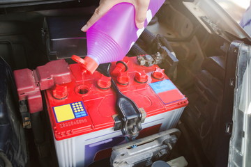 Mechanic hold a bottle of Distilled water for battery and fill for battery in the garage.