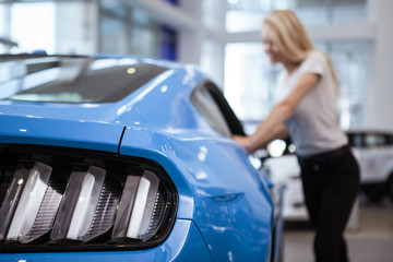 Selective focus on car lights on the foreground, woman looking inside the vehicle on the...