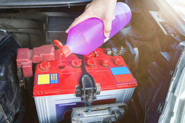 Mechanic hold a bottle of Distilled water for battery and fill for battery in the garage.