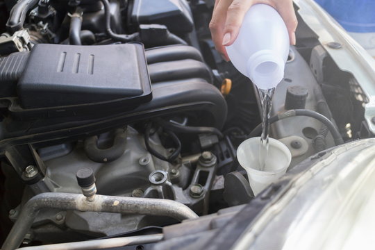 Mechanic filling water for windshield washer fluid to a car in the garage.