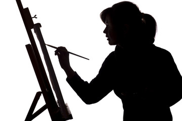 silhouette of a young woman painting on an easel on a white isolated background, the figure of a...