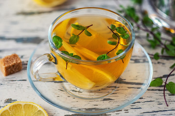 Cup of Lemon tea with lemon slices, cane sugar and mint on light wooden table. Close Up