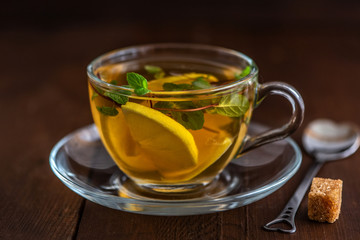 Cup of Lemon tea with lemon slices, cane sugar and mint on dark wooden background