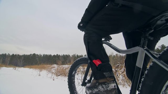 Professional extreme sportsman biker sit a fat bike in outdoors. Cyclist recline in the winter snow forest. Man walk with mountain bicycle with big tire in helmet and glasses. Slow motion in 180fps.