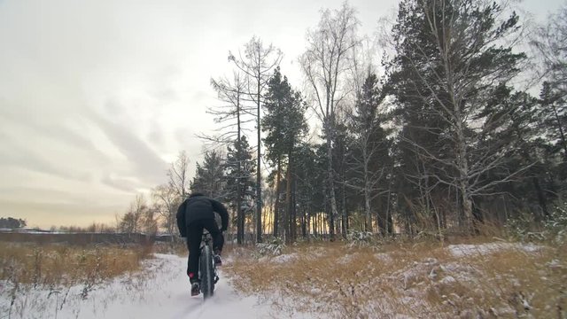 Professional extreme sportsman biker riding fat bike in outdoors. Cyclist ride in winter in snow field, forest. Man does trick on mountain bicycle with big tire in helmet, glasses. Slow motion 180fps.