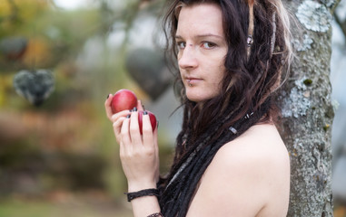 Schöne junge individuelle, exzentrische Frau, mit attraktiven Dreadlocks, Piercing und Tätowierung, die im Garten Eden fordernd den Apfel der Versuchung und Sünde zeigt