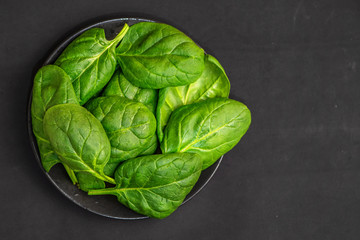 Fresh spinach leaves in bowl on dark background. Top view. With Copy Space