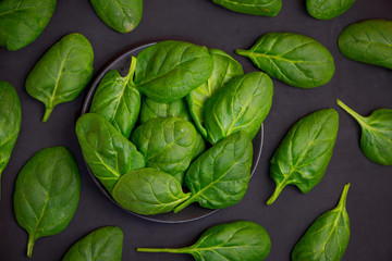 Fresh spinach leaves in bowl on dark background. Top view