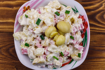 Potato salad with marinated mushrooms, sausage, onion and mayonnaise on wooden table