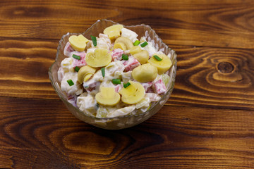 Potato salad with marinated mushrooms, sausage, onion and mayonnaise on wooden table