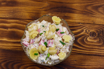 Potato salad with marinated mushrooms, sausage, onion and mayonnaise on wooden table