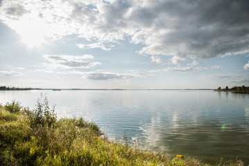 Sunset over the lake in the village with Cumulus clouds and calm water