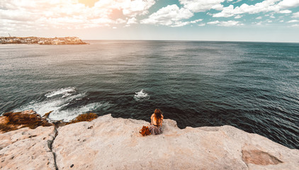 Woman sit on the cliff looking the ocean landscape at sunset. 