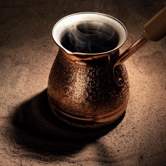 Boiling coffee in copper Turkish coffee brewing pot on the sand