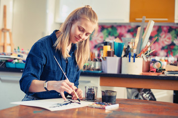 Young Woman Artist Working On Painting In Studio. Selective focus on foreground.