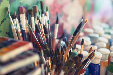 Paint brushes and watercolor paints on the table in a workshop, selective focus, close up.