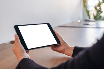 Mockup image of hands holding black tablet pc with blank white screen while sitting in office