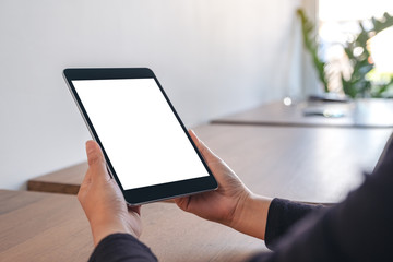 Mockup image of hands holding black tablet pc with blank white screen while sitting in office