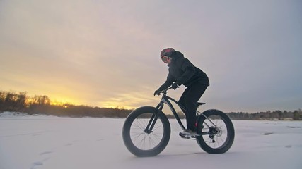 Professional extreme sportsman biker riding fat bike in outdoors. Cyclist ride in winter snow forest. Man does trial trick pedal kick jump on mountain bicycle with big tire in helmet and glasses.